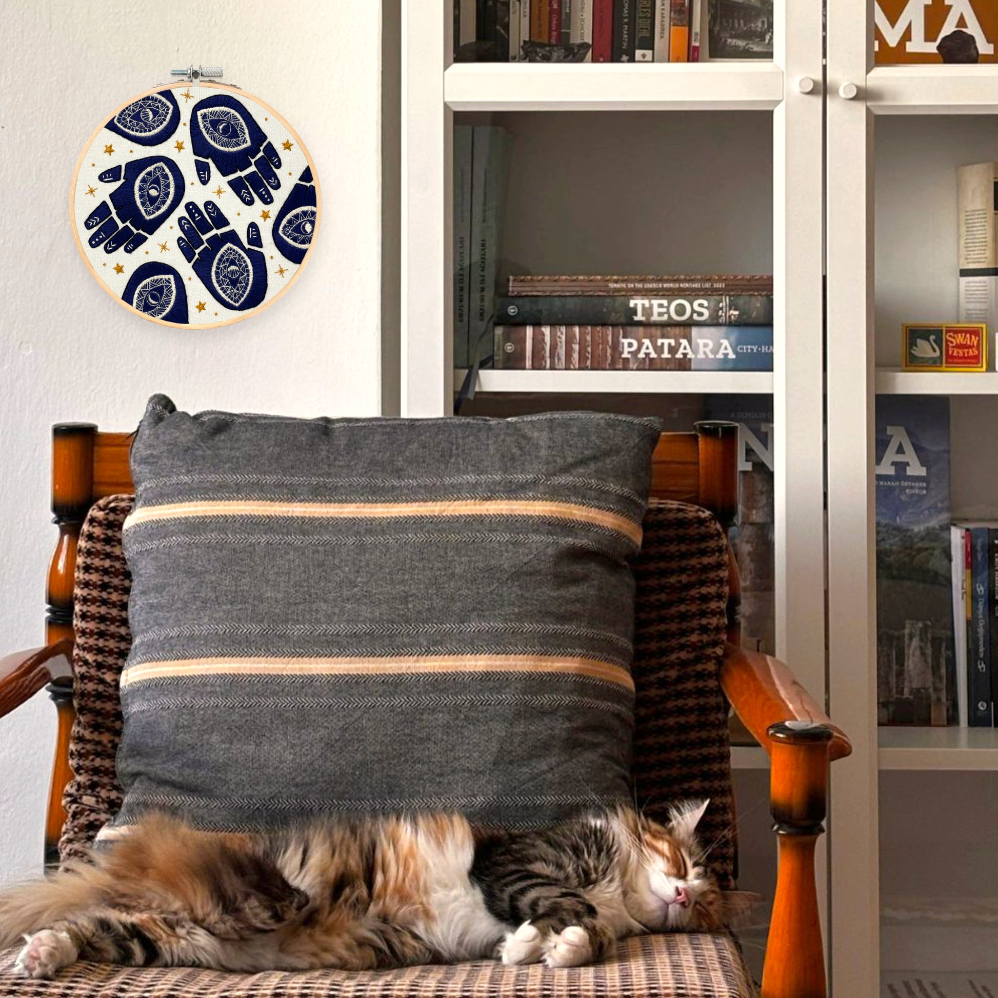 Cat relaxing on a chair with Hamsa Hands Hand Embroidered Hoop Art  on wall
