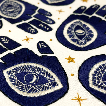 Hand Embroidery Stitches of navy blue hands with white evil eye patterns and gold stars