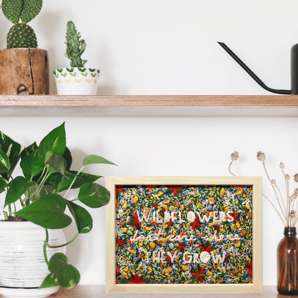 Load image into Gallery viewer, wildflowers don&#39;t care where they grow embroidery design displayed in a frame on a shelf with plants
